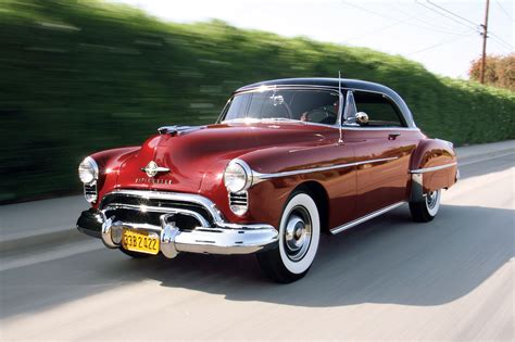 an old red car driving down the road