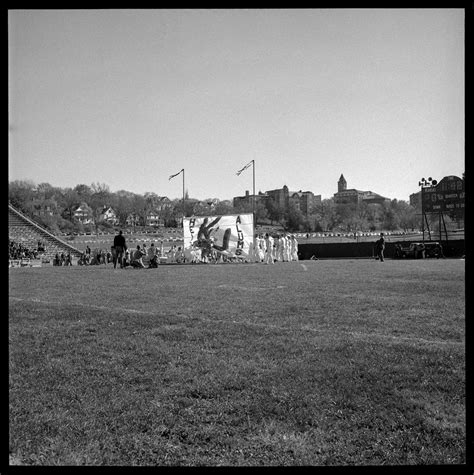 Photograph of KU football players running through a sign at the ...