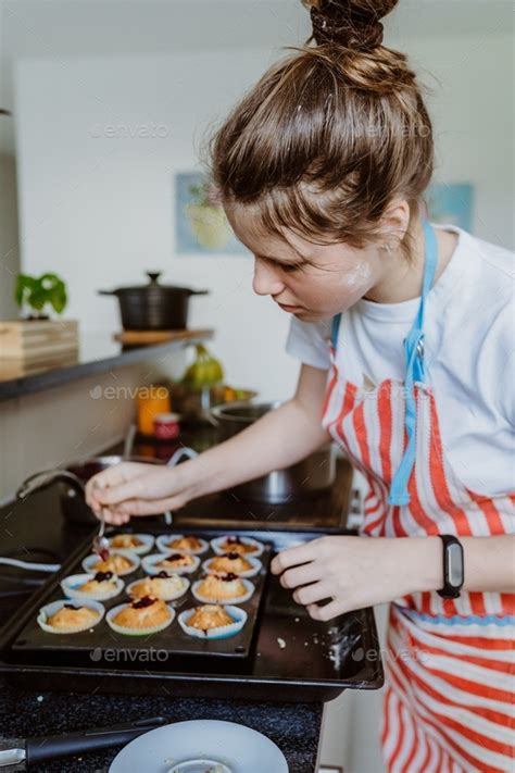 Tween girl making cupcakes with cherry jam at home. Child culinary hobby and leisure activity ...