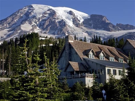 a large house in front of a mountain with snow on it's top and trees around it