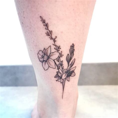 a small flower tattoo on the ankle is shown in black and grey ink, with tiny leaves