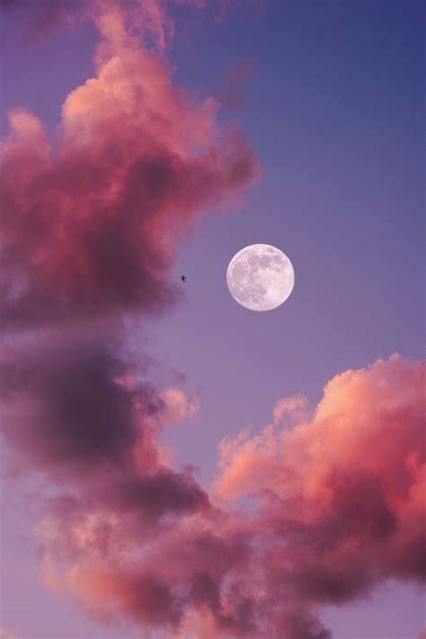 the full moon is seen through some pink clouds