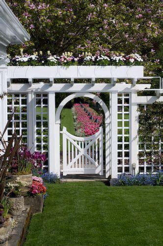 Garden gate and arbor in spring with tulip border, forget me nots, stone urns, planters and ...