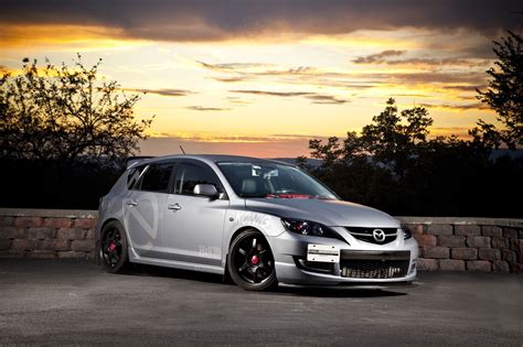 a silver car parked on top of a parking lot next to a stone wall at sunset