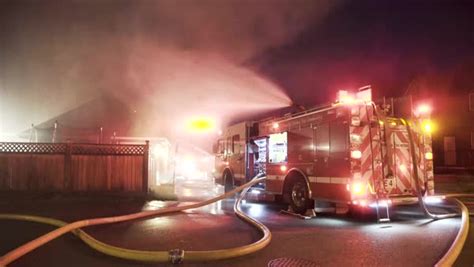 Wide shot of fire truck spraying water on smouldering house at night ...