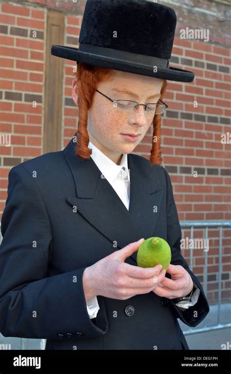 Orthodox religious Jewish boy with red hair & sidelocks examines an esrog for the Sukkot holiday ...