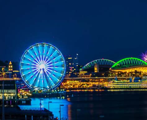 the ferris wheel is lit up at night in front of some buildings and ...