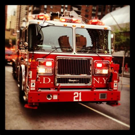 a red fire truck driving down a street with tall buildings in the backgroud