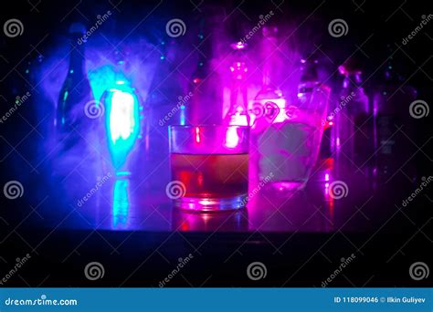 Glass of Whisky on Wooden Bar Closeup with Bottles Blurred View on Dark Background with Light ...