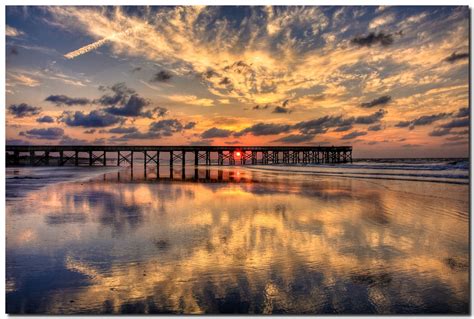 the sun is setting over an ocean with a long pier in the foreground and ...