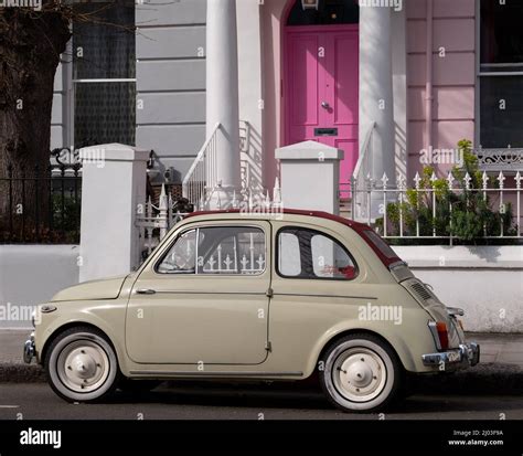 Beige coloured vintage Fiat 500 classic car parked in front of a house with a pink door on a ...