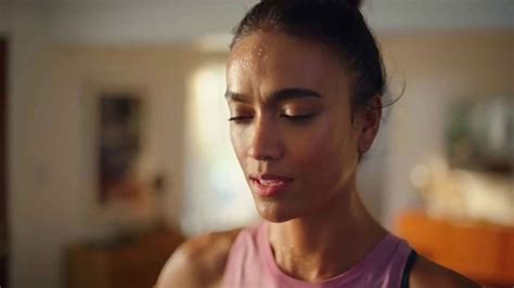 a woman in a pink tank top is looking down at her cell phone and smiling