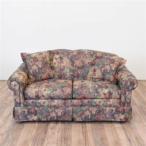 This loveseat is upholstered in a durable floral print fabric in a dark green, red, purple and ...