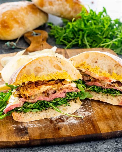 a homemade steak sandwich cut in half on a cutting board.