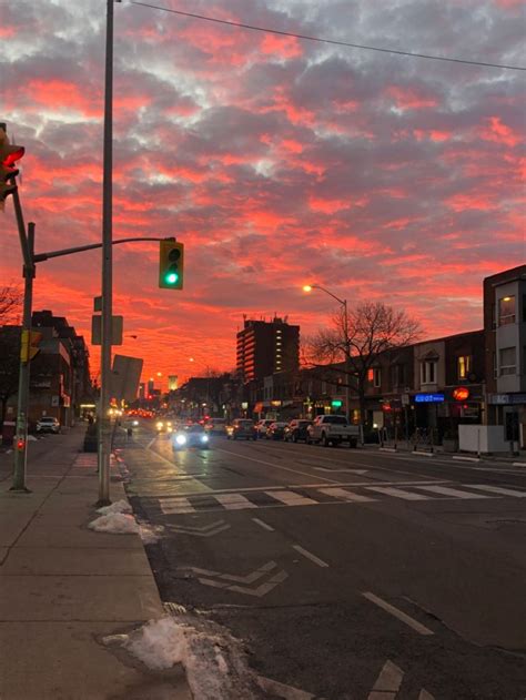 a city street at sunset with cars driving on the road and buildings in the background