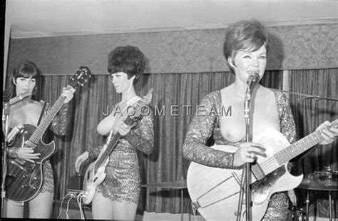 three women singing and playing guitars in front of a microphone while another woman plays the ...