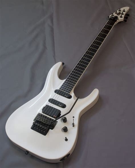 a white electric guitar laying on top of a gray sheet