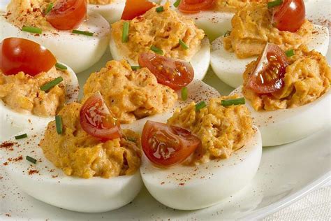 deviled eggs topped with tomatoes and mayonnaise on a white plate, ready to be eaten