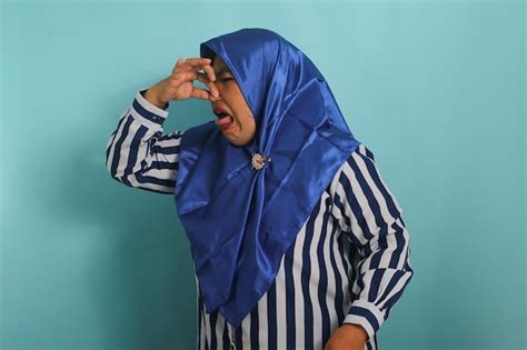 Premium Photo | Asian woman in hijab holds breath pinches nose reacts to stinky bad smell blue ...