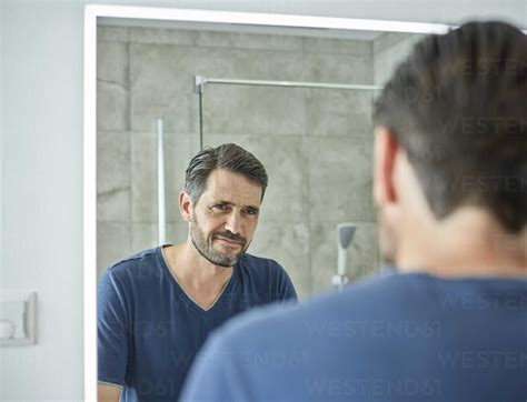 Smiling man looking in bathroom mirror stock photo