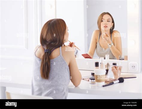 Amazing young woman doing her makeup in front of mirror. Portrait of beautiful girl near ...