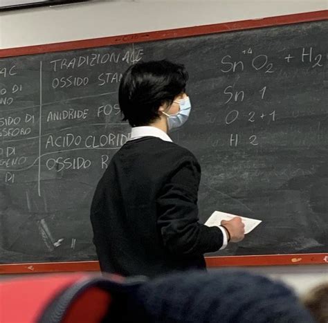 a man wearing a face mask standing in front of a blackboard