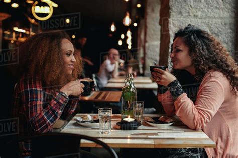 Side view portrait of two young women talking and drinking coffee in a cafe. Female friends in a ...