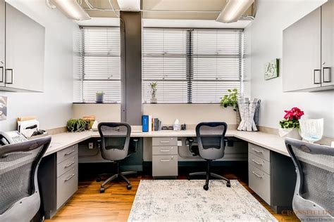 an office with two desks and chairs in front of the window, along with a rug on the floor