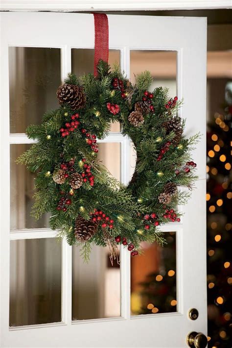 a christmas wreath hanging on the front door with pine cones and red ...