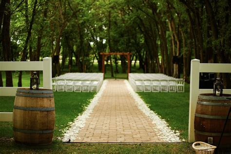 an outdoor ceremony setup with white chairs and wooden barrels at the ...