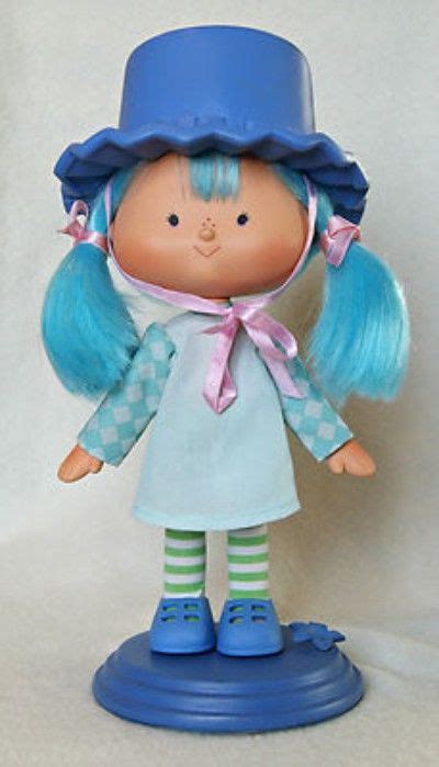 a doll with blue hair wearing a blue hat and green striped socks, standing on a blue base