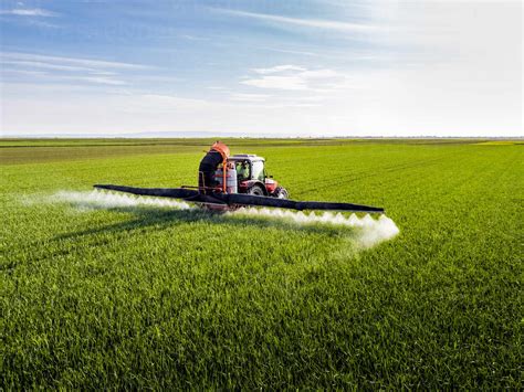 Farmer fertilizing crop through crop sprayer in field stock photo