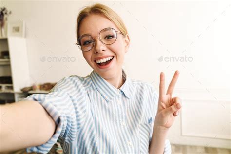 Photo of joyful blonde woman showing peace sign while taking selfie ...