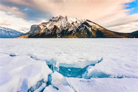 Frozen Lake Minnewanka with rocky mountains and cracked ice from the lake in winter at Banff ...