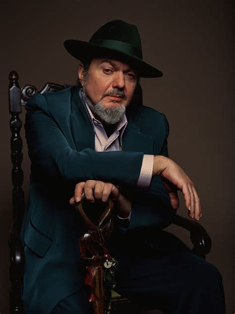 a man in a green suit and hat sitting on a chair with his arms crossed