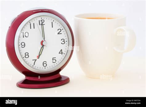 Mug of tea by a red alarm clock at 7 am in the morning just seconds ...