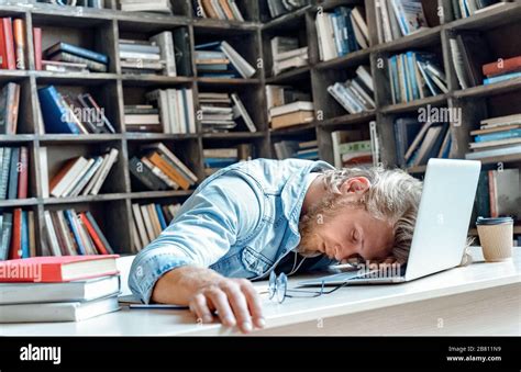 Funny tired sleepy university student sleeping sitting at library desk ...