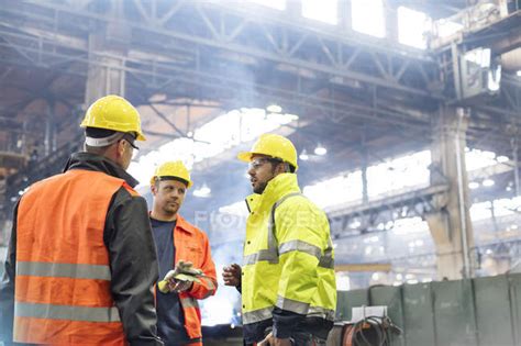 Steel workers talking in factory at work — manufacturing, hi vis ...