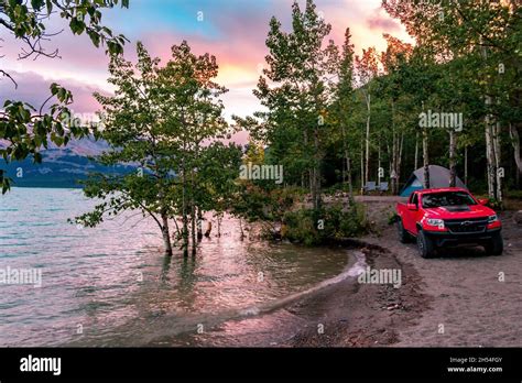 The Perfect camping spot on Abraham Lake with trees, tent and truck infront of sunset lit sky ...