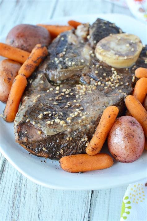 a white plate topped with meat and carrots on top of a wooden table next to potatoes