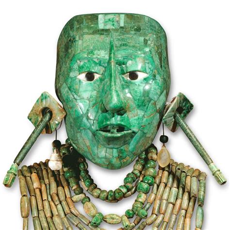 a green mask with long necklaces on it's face and two fingers in the other hand