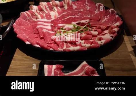 Chinese spicy hotpot soup. Plate with raw meat slides of beef at the table in a restaurant ...