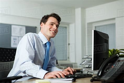 Office worker sitting at desk, smiling - Stock Photo - Dissolve