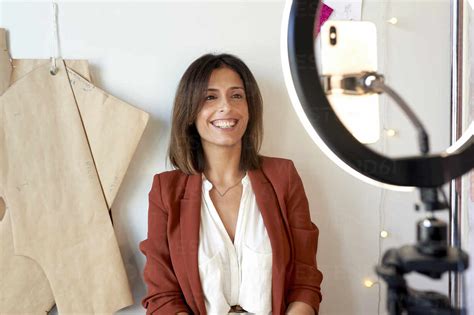 Cheerful fashion vlogger sitting against wall at clothing studio stock photo