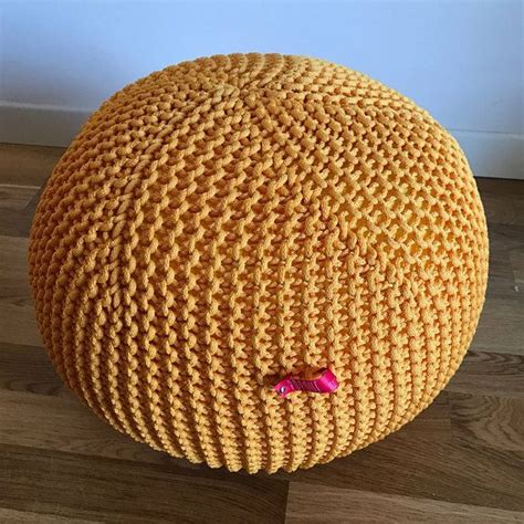 a yellow knitted round poufce sitting on top of a wooden floor
