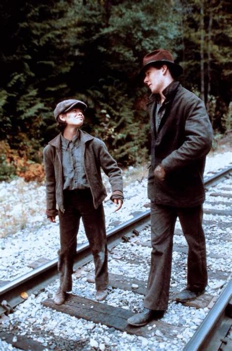 two men are standing on railroad tracks in the snow and one is wearing a hat