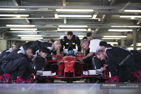 Pit crew preparing formula one race car and driver in repair garage ...