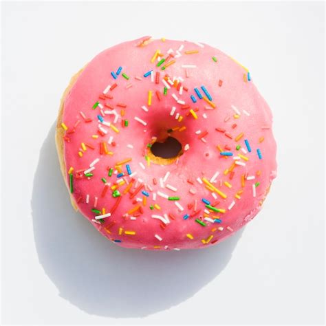 An elevated view of pink donuts with sprinkles on white backdrop | Free Photo