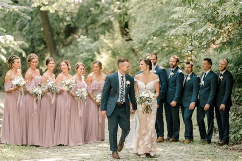 a bride and groom walk with their bridal party in the woods at this wedding