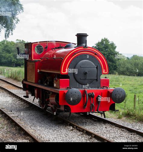 The driver waves from the cab of an industrial 0-4-0 Saddle Tank Steam engine locomotive in red ...